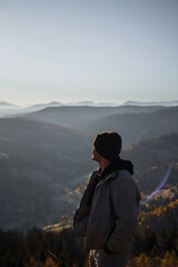 Young man is standing and looking away at the mountains autumn landscape