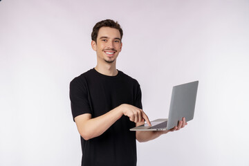 Portrait of young handsome smiling man holding laptop in hands, typing and browsing web pages isolated on white background