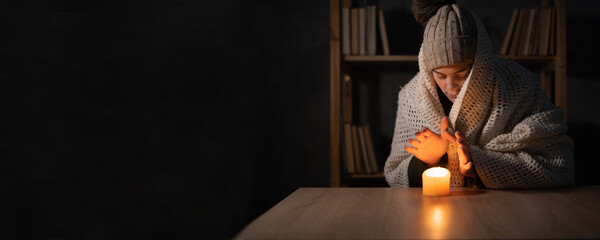 Unhappy woman warm hands on candle at cold home, shutdown of heating and electricity, power outage,...