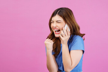 Portrait of happy young woman wearing casual t-shirt talking on mobile phone isolated over pink background