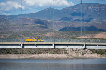 A single yellow dump truck driving across the Roosevelt Lake Bridge