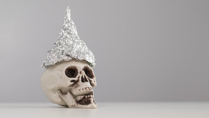 Plastic skull in a tinfoil cap on a white background. Copy space. 
