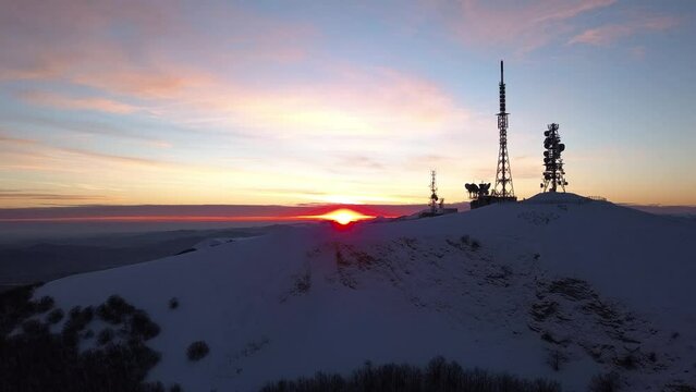 Aerial slow movement around snow covered Nerone mountain with tower during sunset in 4K