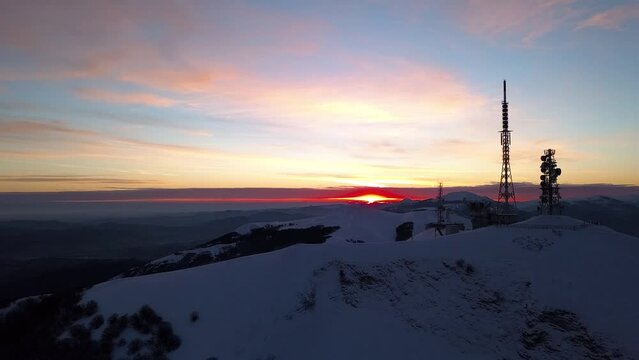 Aerial slow movement around snow covered Nerone mountain with tower during sunset in 4K