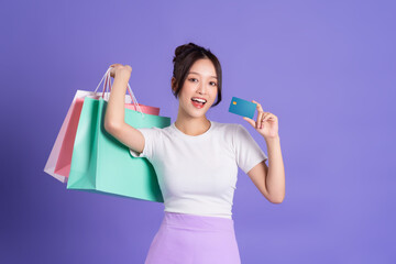 beautiful Asian girl holding shopping bag posing on purple background