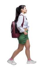 A young girl with a backpack is walking. A pretty brunette with long hair, wearing green shorts and a white shirt. Side view. Full height. Isolated on white background. Vertical.