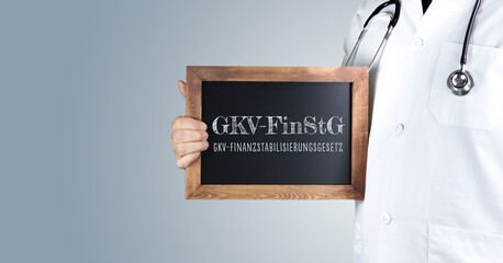 GKV-FinStG (GKV-Finanzstabilisierungsgesetz). Arzt zeigt Begriff auf einem Holz Schild. Handschrift...
