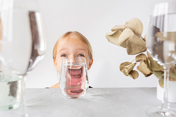 Fashion kid portrait, eye looks through the glass of water. Object distortion, optical illusion...