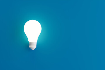 Glowing incandescent light bulb on blue background with copy space.
