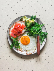 Delicious balanced breakfast - fried egg, salmon sandwich, avocado and arugula on a light background, top view