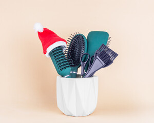 Hairdressing tools and a brush in a Santa Claus hat on a stand on a beige background, front view,...