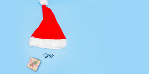 A Christmas card made of a Santa Claus hat, Santa glasses, a New Year's gift on a blue background. Top view, place for text, copy space. Banner