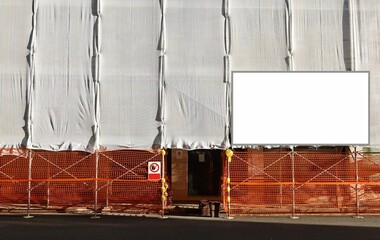 Blank information board on a facade under refurbishment at the roadside. The building is covered  with scaffold sheeting.Background for copy space.