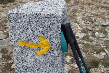 Bastones de marcha nórdica apoyados en un poste de granito. Poste de granito con señal de flecha...