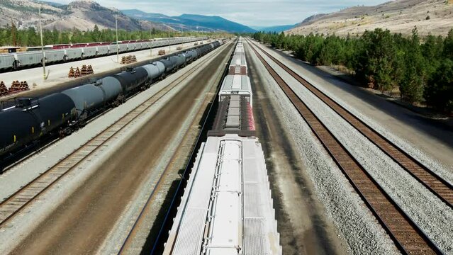 forward flight dolly drone shot flying over a cargo train on a railroad station in a desert environment on a sunny day next to a mountains in the background and powerines in the picture an tank trains