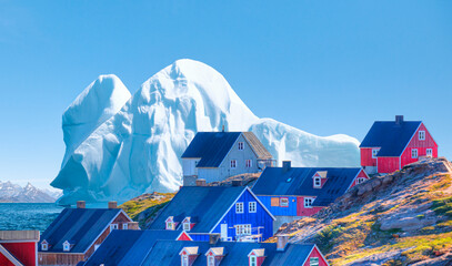 Picturesque village on coast of Greenland a giant iceberg in the background - Colorful houses in...