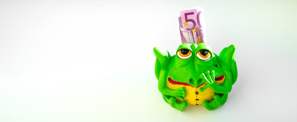 Piggy bank green toad on a white background. Vacation savings. Decorative frog piggy bank for money. A piggy bank with paper money on a white isolate.