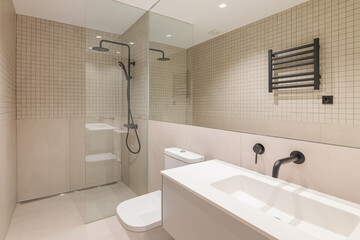 Interior of modern bathroom with huge mirror, beige tiles, shower, black radiator and white sink