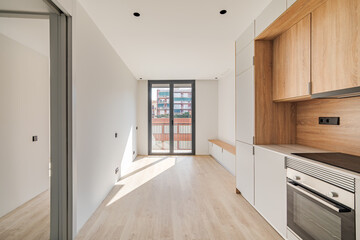 Contemporary minimal kitchen and living room with balcony at empty refurbished apartment. Wooden furniture and modern appliances