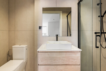Modern bathroom with beige tiles. Square mirror, toilet, white sink and shower zone with glass...