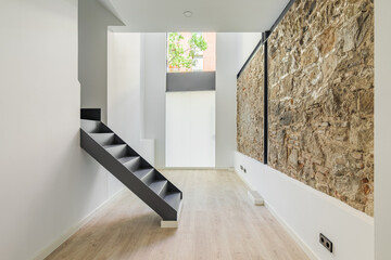 Mix of new and old architecture. Refurbished apartment with restored ancient wall left from old city buildings. Interior of empty renovated room with black stairs leading to second floor.