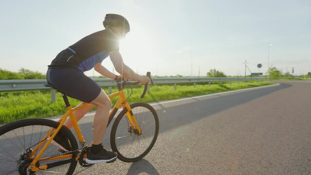 Professional racing biker in sportswear, helmet and sunglasses riding along asphalt road among beautiful green nature. Concept of sport and training.