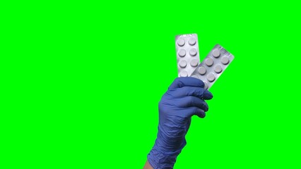 Woman hand in latex blue glove is showing a blisters of pills. Doctor arm in protective medical gloves demonstrating medicines, vitamins, or antibiotics. Close up on green screen background.