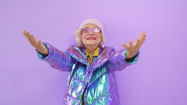 A smiling cheerful elderly lady poses in front of the camera on an isolated purple background. happy woman