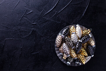 Obraz na płótnie Canvas Glass gold, black, silver decorative cones and golder stars in metallic plate on black textured background. Minimalistic style. Still life. Top view.