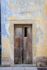 Fototapeta na wymiar Una vecchia porta di legno su un muro scrostato di colore giallo e blu in un vicolo di Castro, borgo del Salento in Puglia