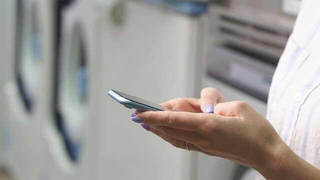 Close-up of a woman's hands holding a smartphone, she uses a smartphone in a public laundry. a picture of women's hands with a smartphone without a face