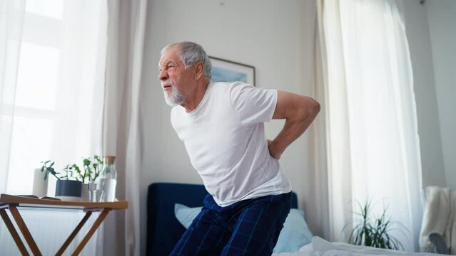 Senior man sitting on bed with back pain.