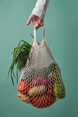 Mesh bag with vegetables and herbs in female hand.