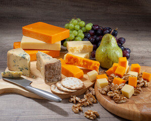 Group shot of assorted cheese on wooden cutting board with biscuits, fruit and nuts