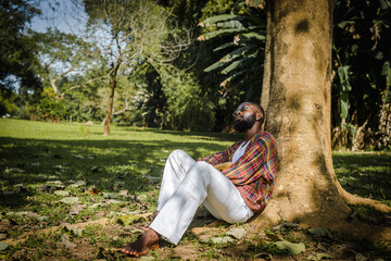 A black man sitting under a tree in a park