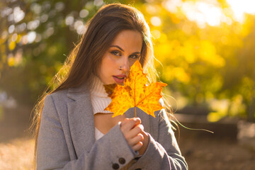 Portrait of a pretty woman enjoying autumn in a park at sunset, with a leaf from the tree