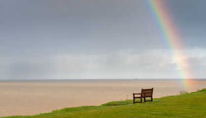 Rainbow over the ocean and wooden bench on the coast for relaxing. Atlantic ocean england