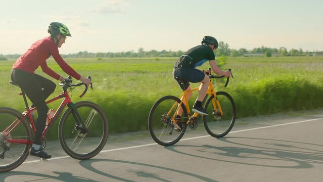 Back view of cyclists pedaling racing bicycles outdoors during sunset. Men in track suits and bicycle helmets enjoying favorite hobby on fresh air.