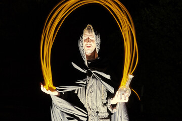 a sorcerer in a black cloak throws fire from palm to palm on a black background Halloween concept