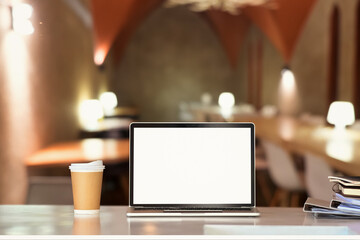 Laptop on white table with blurred restaurant in background. Blank screen for your product display or design montage