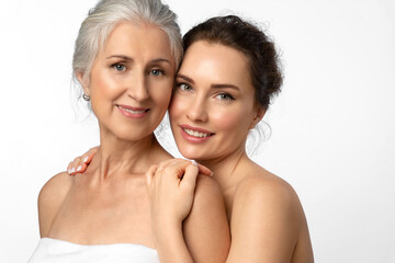 Tender smiling daughter lovingly hugs her elderly mother by the shoulders. Beauty portrait of beautiful women of two generations on white background. - obrazy, fototapety, plakaty