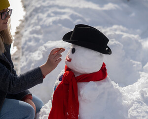 Caucasian woman sculpts a snowman from the snow. The carrot is the place of the nose.