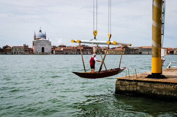 Una gru solleva una barca a remi per portarla in secca con il vogatore a bordo lungo il canale della Giudecca a Venezia