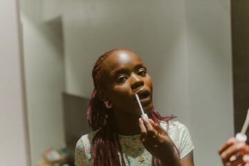 A black woman applying lip gloss