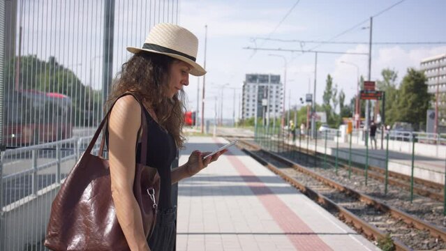 Young woman waiting for public transport, looking at mobile phone.