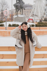 Beautiful caucasian woman in warm cozy clothes skating on ice rink as snow falls. Cold happy winter day in festive city. Holidays, Christmas, New Year, beauty concept.