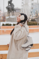 Obraz premium Beautiful caucasian woman in warm cozy clothes skating on ice rink as snow falls. Cold happy winter day in festive city. Holidays, Christmas, New Year, beauty concept.
