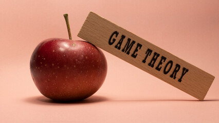 Game theory writing on wooden surface. Apple pink background concept.