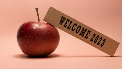 Welcome 2023 lettering on wooden surface. Apple pink background concept.
