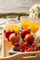 still life reading, breakfast or picnic by the water in the open air with flowers, fruit, orange juice 